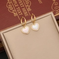 Golden hoop earrings with pearl heart pendants displayed on a vintage book - Earrings / Gold