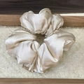 Detail of a champagne satin scrunchie with a silky texture on a glass plate - Champagne