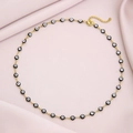 Gold evil eye necklace with black and white beads on soft pink fabric background - Black
