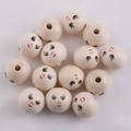 Macro shot of 20mm natural wood beads with smiling face patterns on white fabric - Long Eyelash Girl