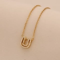 Macro shot of gold U-letter pendant necklace with embedded zircon on beige fabric - Letter U
