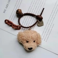 Detail eines Teddyhund-Schlüsselanhängers mit braunem Seil, Metallglocke und Herzanhänger - Beigefarbener Teddy-Anhänger