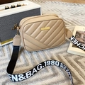 Quilted beige camera bag with a black and white woven strap on a stylish textured rug - Khaki