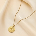 Gold stainless steel necklace with Pisces zodiac coin pendant on soft beige fabric - Pisces