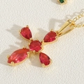 Macro detail of a golden cross pendant featuring vibrant red zircon gemstones on white texture - Rose Red Zirconia Cross