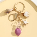 Detail of beach theme keychain with seashells and starfish charms on a golden metal ring - Fuschia