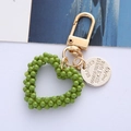 Dettaglio portachiavi a cuore verde con finiture dorate e targhetta in metallo incisa - Confezione in busta singola OPP / Cuore di Perla Verde Militare