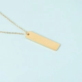 Primer plano detallado del colgante rectangular de oro pulido sobre fondo azul claro - Dorado