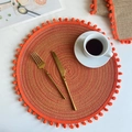 Macro detail of round orange woven placemat with ball fringe and golden cutlery set - 38cm Placemat / Orange