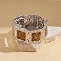 Detailed close-up of retro silver bangle with orange enamel spiral patterns on mineral rock - Brown