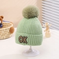 Detail of light green knit hat with a large fluffy pom-pom and OK patch on a white stand - One Size (2-5 Years) / Green