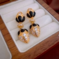 Makro-Detail von Vintage-Goldohrringen mit schwarzem Emaille und Zirkon in einer Schmuckbox - Goldene Zirkon Wassertropfen Ohrringe (Silbernadel)