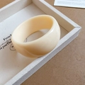 Vista detallada de un brazalete ancho de acrílico crema sobre bandeja decorativa - Blanco Crema