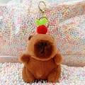 Plush brown capybara keychain with red fruit hat on a colorful pastel background - Dark Brown Apple + Gold Clip