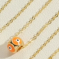 Detailaufnahme einer goldenen Halskette mit orangefarbenem Emaille-Böse-Auge-Anhänger - Orange