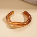 Primer plano de un brazalete de resina ámbar translúcida sobre un fondo beige estético - Marrón