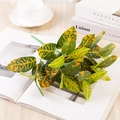 Artificial Croton plant branch with yellow variegated leaves on an open book - Variegated Croton