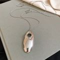 Macro shot of large silver oval hollow pendant on textured book with soft silk fabric - Silver Pendant with Silver Fine Chain
