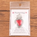 Red enamel pocket hug heart pendant with sentimental card on a rustic wood background - Hollow Lace Red Heart