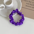 Elegant purple satin hair scrunchie with smooth silk texture on a white ceramic plate - Purple