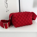 Red popcorn textured crossbody bag with adjustable wide strap shown on white podium - Burgundy