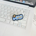 Close-up of a blue plush embroidery pin with a smiley face on a white keyboard - Mea Culpa Blue