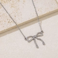 Detail of silver bow pendant with round beads on cross chain against beige stone surface - Liquid Metal Bow Knot (NKS-002_05A)