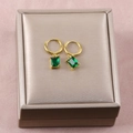 Primer plano de pendientes dorados con cristales verdes rectangulares sobre caja - 26b06021-green diamond earrings
