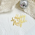Detailed view of a gold Happy New Year acrylic cake topper on a white textured backdrop - Happy New Year / Gold