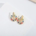 Detail of gold earrings with multicolored zircon stones on white stone background - Colorful