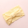 Detail of light yellow knitted baby headband featuring a large bow on pink background - Beige