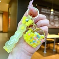 Close-up of yellow heart-shaped acrylic keychain with liquid sand and Fairy Tales wristband - Yellow Bow With Glow-in-the-dark Bubble Beads And Heart Shape