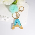 Detail of resin letter A keychain with blue stones, gold glitter, and mint pompom - Letter A
