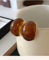 Close-up of amber C-shaped earrings with gold trim hanging on a ceramic cup - Oval Edged Studs (131#) / Amber Gold