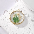 Macro detail of round gold pendant with real white daisy flowers and gold foil flakes - May Lily of the Valley With Gold Foil
