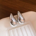 Macro close-up of silver-toned teardrop earrings on a white ceramic display tray - Silver