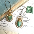 Macro detail of vintage beetle earrings with green enamel wings on an old letter background - Scarab Beetle Shape / Green/Antique Gold
