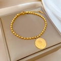 Makroaufnahme eines Kugelarmbands aus Titanstahl mit einem Vintage-Goldmünzenanhänger - Titanstahl / Gold