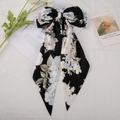 Vue détaillée du nœud à cheveux en satin noir fleuri avec long ruban sur fond texturé - Fleur noire