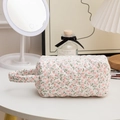 Close-up of quilted cotton cosmetic bag with floral pattern and secure zipper closure - Handheld Pink Floral