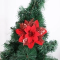 Nahaufnahme einer roten Glitzer-Weihnachtsblume am Zweig eines grünen Weihnachtsbaums - Rot mit braunem Blatt
