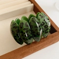 Close-up of a wide green leopard print resin cuff bracelet on a brown jewelry box - Green