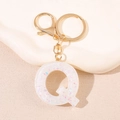 Porte-clés doré avec lettre Q en résine et paillettes irisées sur surface beige texturée - Lettre Q