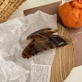 Détail d'une grande pince à cheveux marron écaille de tortue sur un plateau en bois - Café Foncé