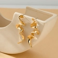 Modern gold twisted ribbon earrings displayed on a minimalist beige ceramic stand - Spiral Fluid Ribbon / Gold