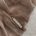 Detail van barokke parel haarclip met gouden legering op getextureerde stoffen achtergrond - Kleine Bloem