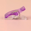 Side view of a purple transparent sewing clip with a metal spring on a pink background - Purple