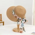 Detail of a straw sun hat with a floral print ribbon on a wooden stand - Little Peach Hat Khaki