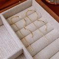 Detailed close-up of golden wavy chain threader earrings on a beige jewelry box - Gold Wave Chain Ear Lines
