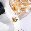 Detailed macro view of gold butterfly pendant with rainbow crystals on white silk - Multicolor
